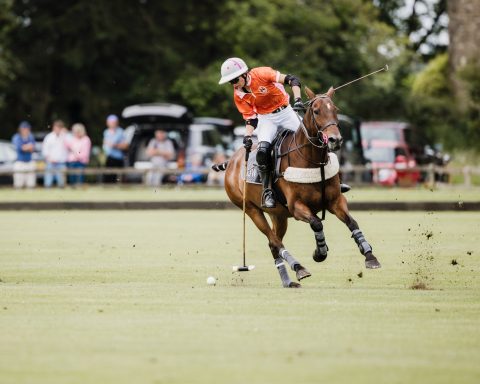 Match action Polo player in an orange shirt leaning forward on horseback during play