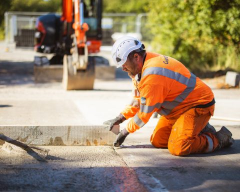 Road construction Construction worker in orange high-visibility clothing finishing a concrete surface
