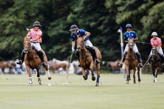 Team pursuit Polo players in pink and blue shirts galloping together during a match